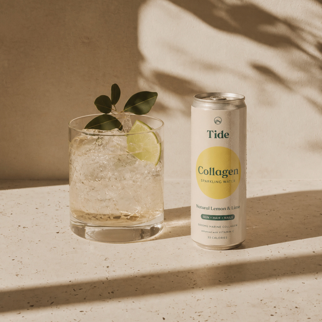 A can of Tide Collagen Sparkling Water stands next to a glass of iced drink garnished with a lime wedge and green leaves, set on a textured beige surface with warm natural shadows.
