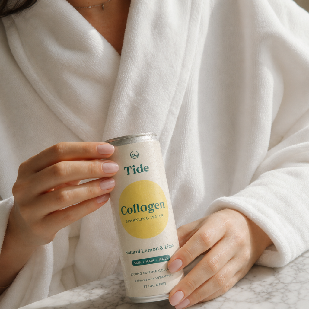A person in a white robe holds a can of Tide Collagen Sparkling Water in Natural Lemon & Lime flavor. The can features a cream-colored label with a prominent yellow circle and green text, set against a soft, warm background.