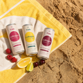 Three Tide Collagen beverage cans arranged on a yellow-and-white towel on sandy ground, with raspberries, a lemon slice, and a lime nearby. The cans show flavors: Collagen Lemon & Lime, Collagen Sparkling Cherry, and Collagen Wild Berry Raspberry.